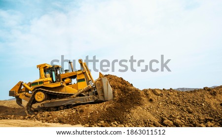Bulldozer at a construction site shovels mountain soil into a heap Royalty-Free Stock Photo #1863011512