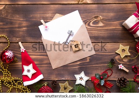 Christmas flat lay on a wooden background with keys to new house in the center with a envelope with a note sheet. New year, transfer, shares of the mortgage, the rental of a cottage. Space for text