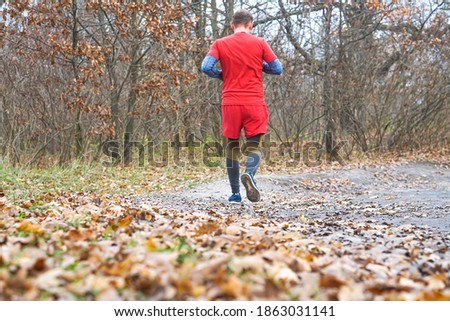 back view of young sport man with strong calves muscle running outdoors in off road trail trees track under beautiful Autumn sunlight in fitness, countryside training and healthy lifestyle concept