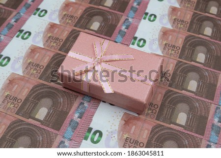 Pink gift box lies on 10 Euro banknotes lined up in a row. Close-up