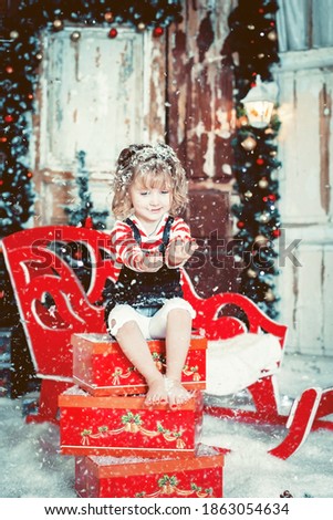 A little girl sits on boxes with New Year's gifts and catches the falling snow. Selective focus image