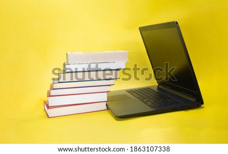 Laptop and stack of different books on yellow background