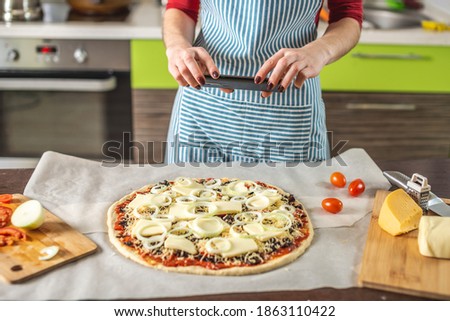 A female chef blogger takes photos of home-made pizza on her phone. The concept of food photography for social networks