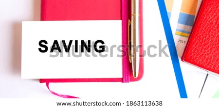 Text SAVING on white card lying on notepad on office desk. Financial concept.