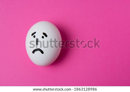 An egg with a sad face, on a pink background with copy space.