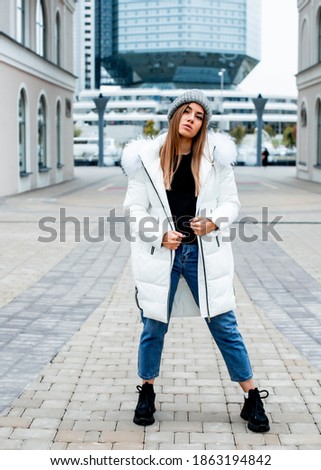 beautiful girl of European appearance posing in a warm white jacket and jeans, fashionable style