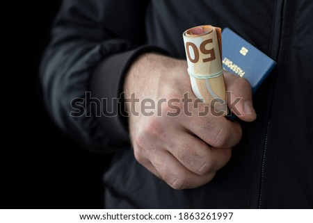 Passport and cash in male hand on black background. Illegal migration concept. Royalty-Free Stock Photo #1863261997
