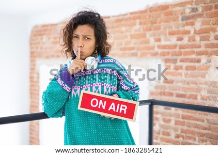 Portrait of a young and exotic woman begging for silence. She holds in her hand a sign with the text On Air. Space for text.