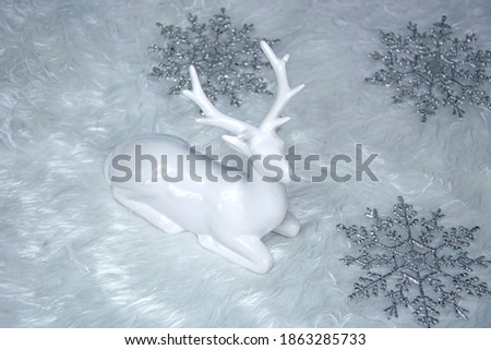 White deer in the Christmas decor. Snowflakes lie on the white fur carpet. Preparing for Christmas 2021.