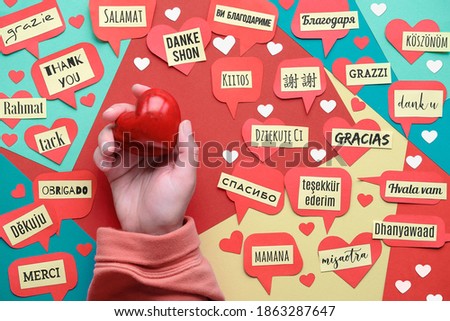 Thank You in many languages. Paper art, creative flat lay, top view on paper tags. International Thank you day. Creative background on colored paper. Hand with stone heart.