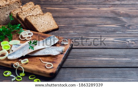 Herring fillet with parsley and onions on a cutting board, dark wooden background with place for text. Traditional Norwegian or Danish smorrebrod ingredients. Herring sandwich, healthy food concept.
