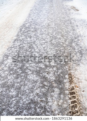 slippery ice-covered city road with car tire tread imprint after freezing rain on cold autumn day