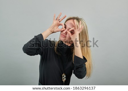 Making glasses of fingers, looking at camera and smiling, funny, hold hands near eyes, imitating binoculars, holding arm eyebrows, through imaginary binocular, grimacing, mask with hand.