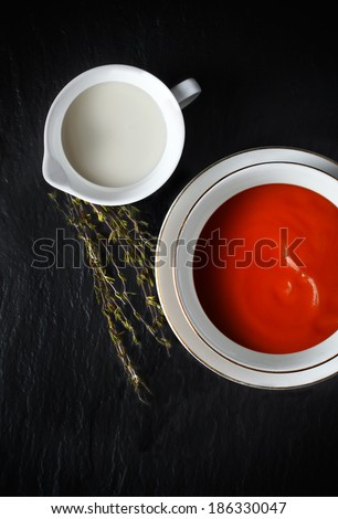Overhead shot of fresh tomato soup with single cream and thyme herbs. Selective lighting. Copy space.