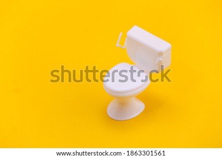 Mini white toilet on yellow background. Minimalism. Top view