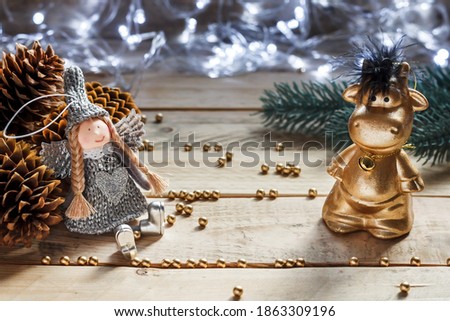 Christmas toy angel, big cones, New Year's toy bull with decor inside on a wooden background. Blurred garland and fir branch on the background. Christmas card concept. Background for Happy New Year.