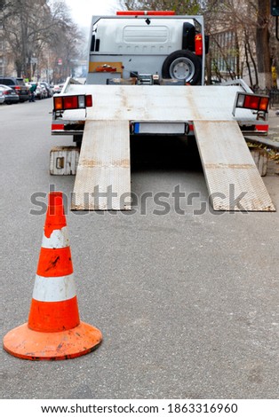 A bright orange traffic cone stands on the dark asphalt and fences the roadway with a parked transport truck, vertical image, copy space.