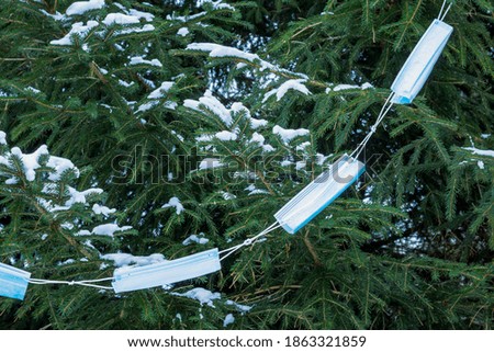 A garland of medical masks decorates the spruce trees with snow. New year and christmas concept amid coronavirus restrictions