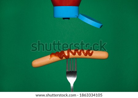 Sausage on a fork sprinkled with ketchup in a close-up view from the front on a green background