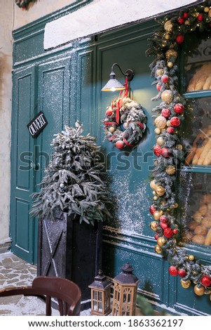 Bakery showcase christmas decorations. Stylish wreath with red, gold baubles and festive lights, covered snow, front of store at market, city street. Copy space. christmas, seasonal greetings concepts
