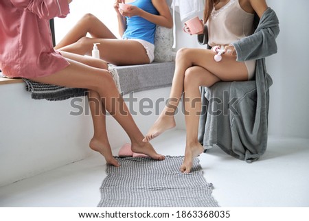 Cropped photo of legs of three attractive girls doing skin care procedures at home. Slim female sitting at the chair during the lymphatic drainage massage