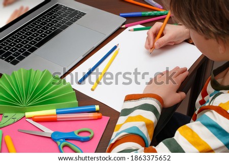 The boy age 8-9 years old is learning online to draw at home. On table are laptop and art supplies. Distance learning and self-isolation concept. 