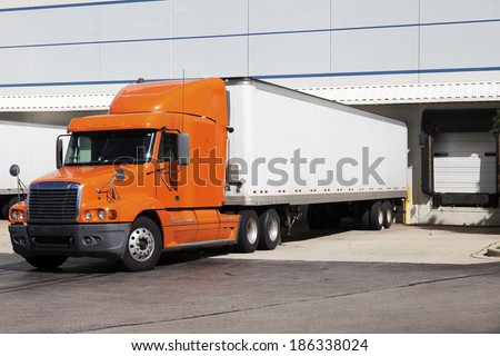Orange semi truck by the door of warehouse Royalty-Free Stock Photo #186338024