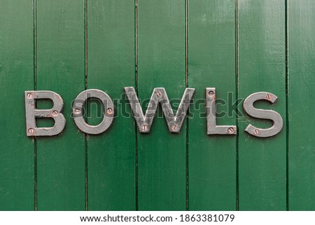 Old BOWLS sign on a dark green painted wooden fence. Bowls is a relaxed pursuit, usually played in rural British villages.