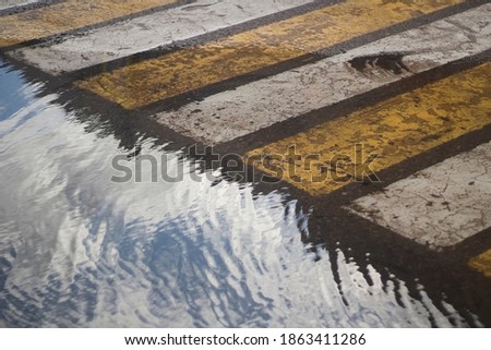 Puddle at the crosswalk. Road in the city. Road markings on the street. White and yellow stripes for pedestrian traffic safety. A puddle on the asphalt.