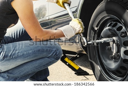 Woman is changing  tire of her car with wheel wrench.