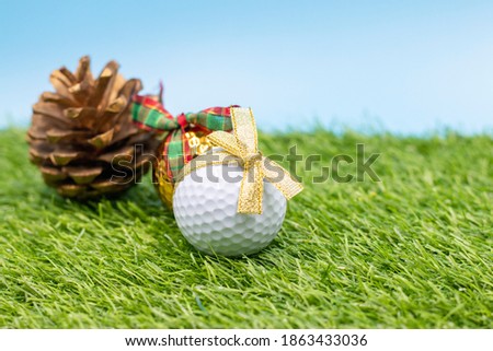 Golf ball with golden ribbon on green grass with Christmas ornament
