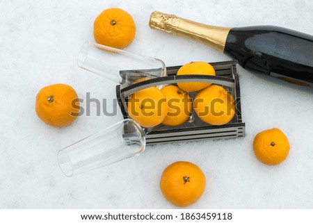 A bottle of champagne and a wooden box with tangerines in the snow. Christmas treat.