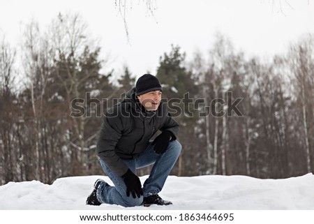 A man in winter clothes is on one knee in the snow playing with children. Family pastime