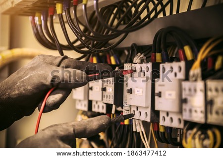 Close-up hand of electrical engineer using measuring equipment to checking electric current voltage at circuit breaker and cable wiring system for maintenance in main power distribution board. Royalty-Free Stock Photo #1863477412