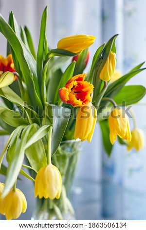 A bouquet of red and yellow tulips stands in a glass vase on the table. Vertical image. Selective focus, blurred background.