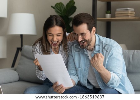 Excited young couple triumph reading amazing unexpected offer or deal in post paper correspondence. Overjoyed man and woman feel euphoric with good message or news in postal paperwork letter. Royalty-Free Stock Photo #1863519637