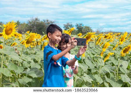 Asian little children are brother and sister used mobile phone taking a selfie while going to sunflower field. 