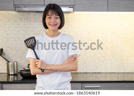 Asian woman crossed arms And standing in the kitchen of the house holding a spatula