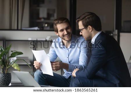 Friendly elder male employee mentor leader explaining paperwork to younger newbie colleague intern in modern office space, capable millennial lawyer assistant convincing customer in profits of deal Royalty-Free Stock Photo #1863565261