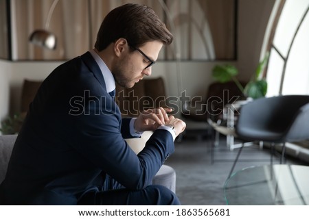 Time management. Serious male employee looking at wrist watch checking time waiting for hr invitation on job interview, punctual young businessman expecting partner who is late for meeting in office Royalty-Free Stock Photo #1863565681