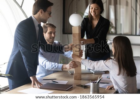 Happy excited multiethnic business team leaded by professional mentor coach participating in teambuilding activity playing educational game building tall column from cubes supporting helping coworkers Royalty-Free Stock Photo #1863565954