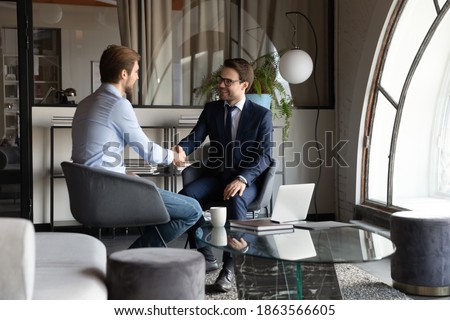 Happy satisfied millennial men client and insurance broker handshaking after signing deal, friendly boss getting acquainted with new worker, young male intern thanking colleague mentor for assistance