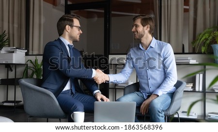 Two happy male business partners handshaking reaching agreement on negotiations, smiling leader greeting skilled capable worker employee with reward promotion, content client and banker finishing deal Royalty-Free Stock Photo #1863568396