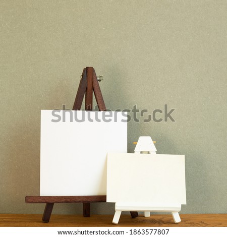 Easel with blank canvas on wooden desk. Khaki green background