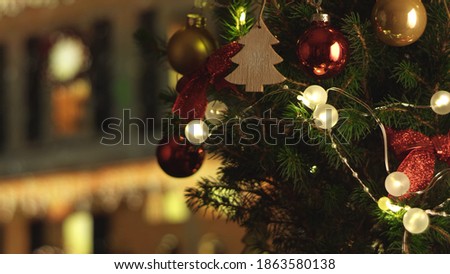New Years Christmas festive background with Christmas house on the background. Christmas tree. Decorations, red gold balls and glowing bulbs on the tree. Warm home mood. Depth of field, soft focus