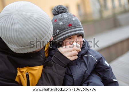 closeup portrait of  man helping to blow nose of his little son wearing winter jacket and knit hat. Image with selective focus