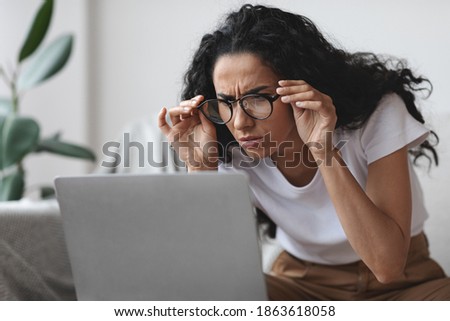 Young woman freelancer with bad eyesight using laptop, trying to work from home, copy space. Curly lady holding her glasses and squinting, looking at laptop screen, having vision troubles Royalty-Free Stock Photo #1863618058