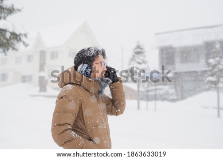 Asian man using  smartphone on city street during snowfall in winter.