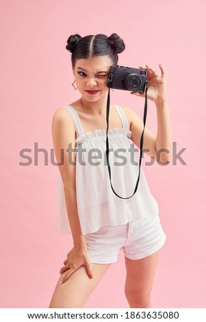 Portrait of beautiful young Asian traveler taking photo with camera over pink background. 
