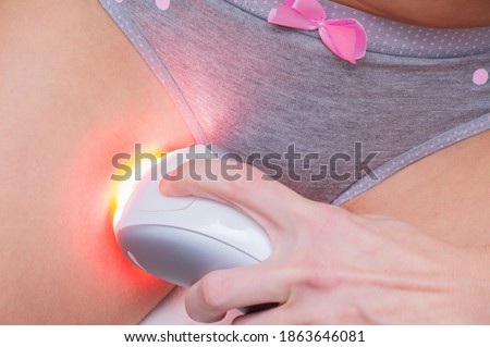 Young woman with a IPL laser hair removal device shaving her bikini line. Removing unwanted hair and using the pulsed light epilator at home.